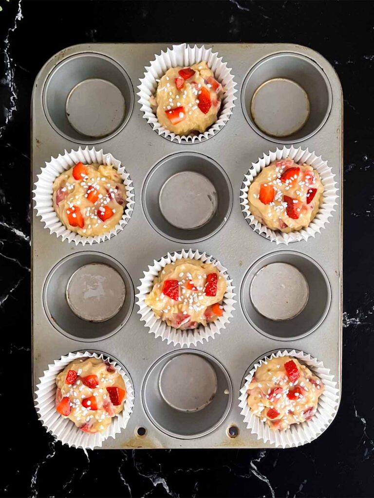 Strawberry muffin batter divided into six paper lined muffin cups and sprinkled with pearl sugar.