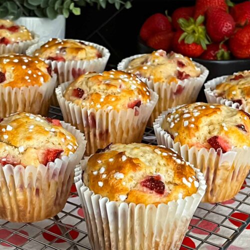 Strawberry muffins on a wire cooling rack on a dark surface.