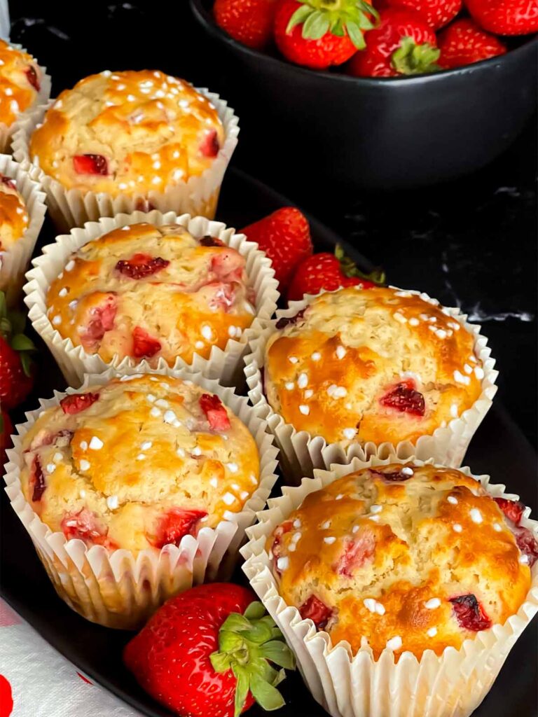 Strawberry muffins on dark oval platter garnished with fresh whole strawberries.