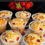 Strawberry muffins on a wire cooling rack on a dark surface.