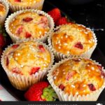 Strawberry muffins on an oval dark plate on a dark surface garnished with fresh whole strawberries.