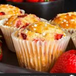 Strawberry muffins on an oval dark plate on a dark surface garnished with fresh whole strawberries.