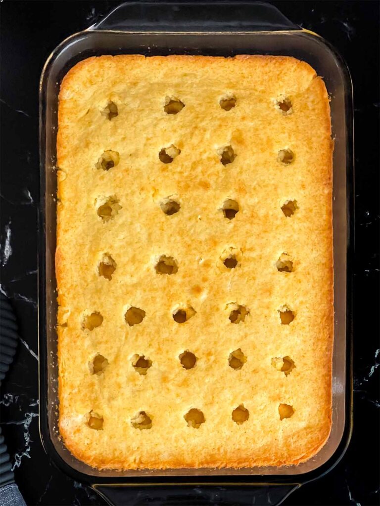 Baked cake with holes poked in it for the berry poke cake recipe.