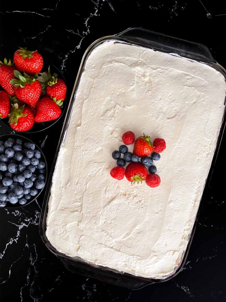 whipped cream cheese frosting and garnished with strawberries, raspberries, and blueberries.