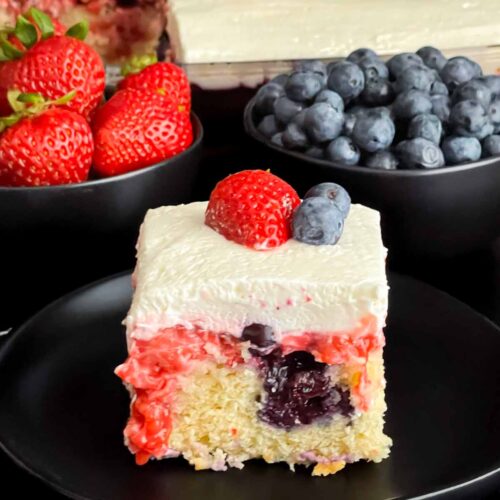 A slice of berry poke cake on a dark plate.