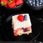 A slice of berry poke cake on a dark plate.