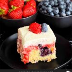 A slice of berry poke cake on a dark plate.