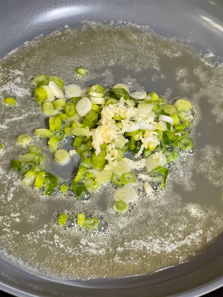 Green onions and garlic cooking in butter and oil in a skillet.