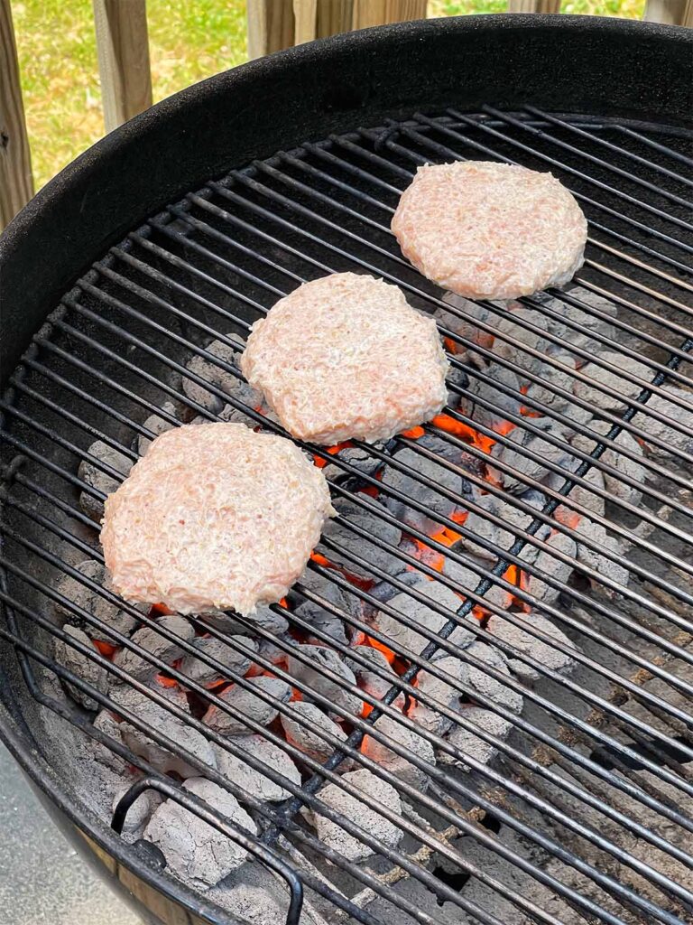 Chicken burgers cooking on a charcoal grill.