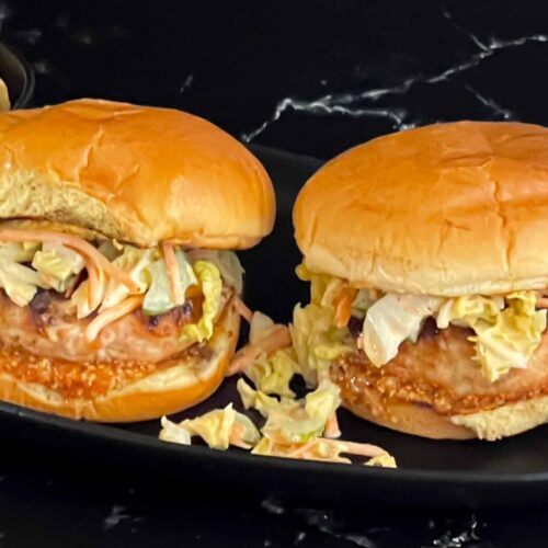 Grilled Carolina chicken burgers on a black plate.