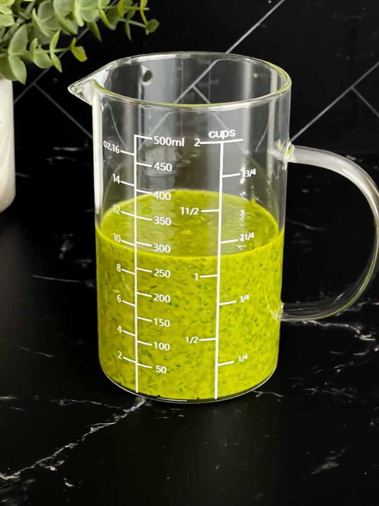 Herb vinaigrette in a glass measuring cup on a dark surface.