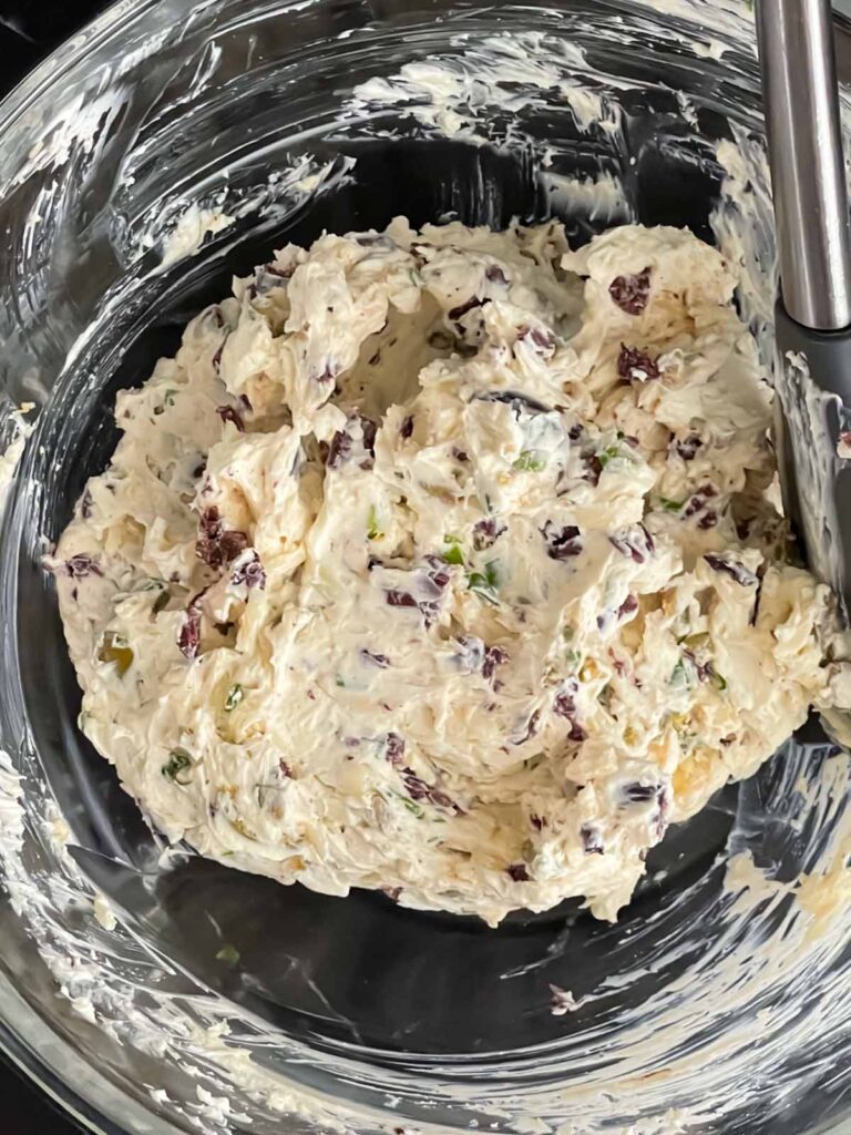 Olive cheese ball ingredients blended together in a glass mixing bowl.