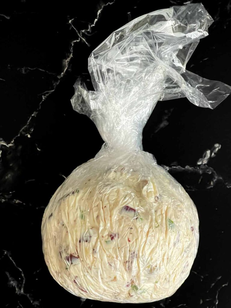 Olive cheese ball formed in plastic wrap on a dark surface.