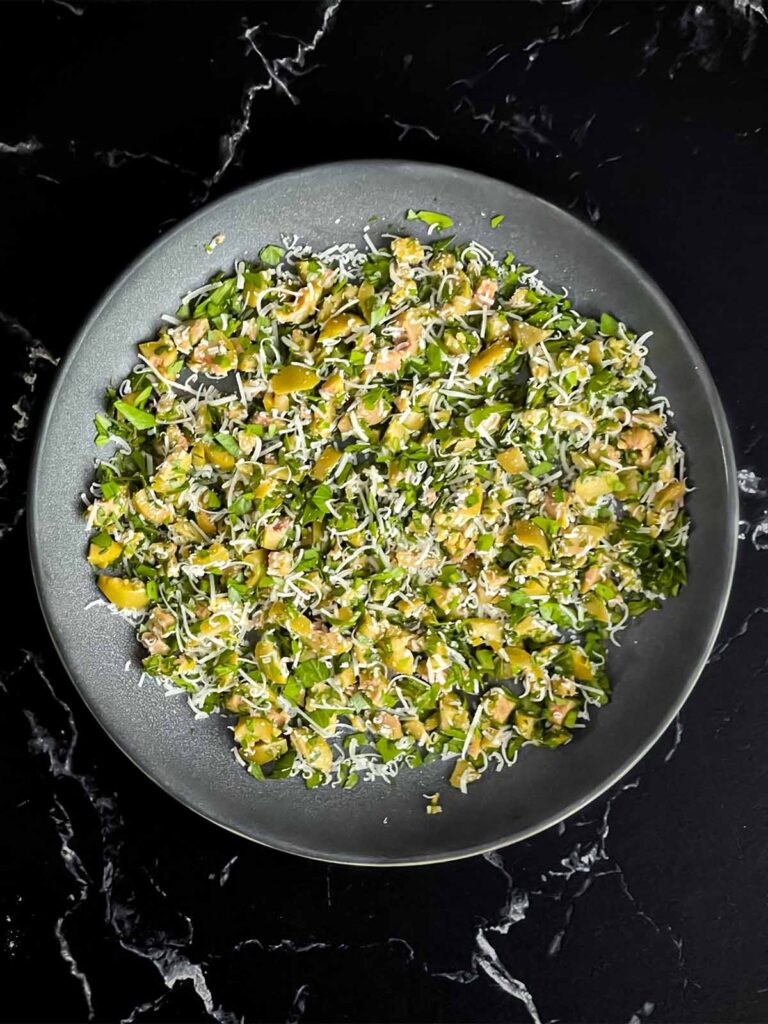 Olive cheese ball coating ingredients mixed in a shallow bowl on a dark surface.