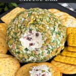 Olive cheese ball on a dark plate surrounded by different shaped crackers.