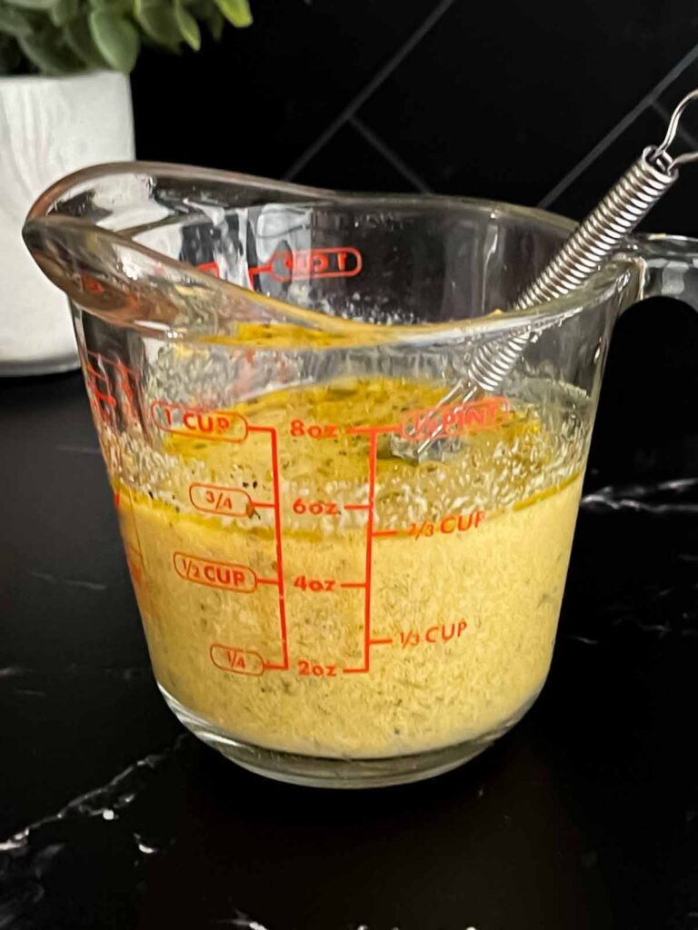 Lemon herb orzo pasta salad mixed in a glass measuring cup on a dark surface.