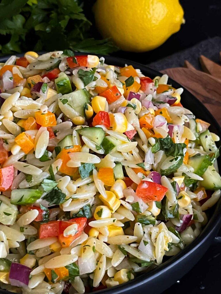 Orzo pasta salad in a dark bowl on a dark surface.