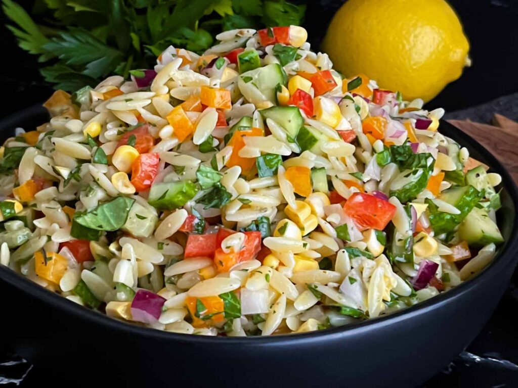 Orzo pasta salad in a dark bowl on a dark surface.