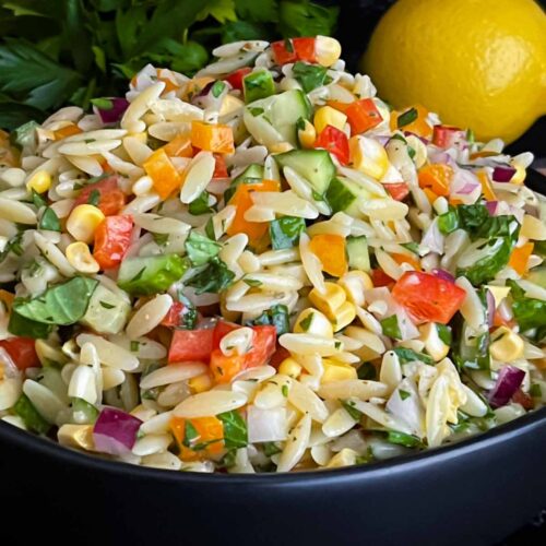 Orzo pasta salad in a dark bowl on a dark surface.