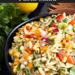 Orzo pasta salad in a dark bowl on a dark surface.