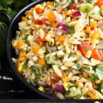 Orzo pasta salad in a dark bowl on a dark surface.