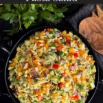 Orzo pasta salad in a dark bowl on a dark surface.