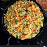 Orzo pasta salad in a dark bowl on a dark surface.