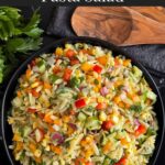 Orzo pasta salad in a dark bowl on a dark surface.