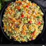 Orzo pasta salad in a dark bowl on a dark surface.