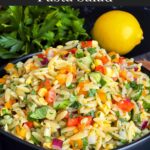 Orzo pasta salad in a dark bowl on a dark surface.