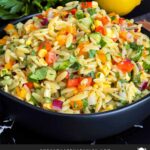 Orzo pasta salad in a dark bowl on a dark surface.