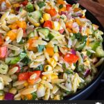 Orzo pasta salad in a dark bowl on a dark surface.