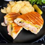 Grilled Cuban Pork Tenderloin Panini on a black plate with chips.