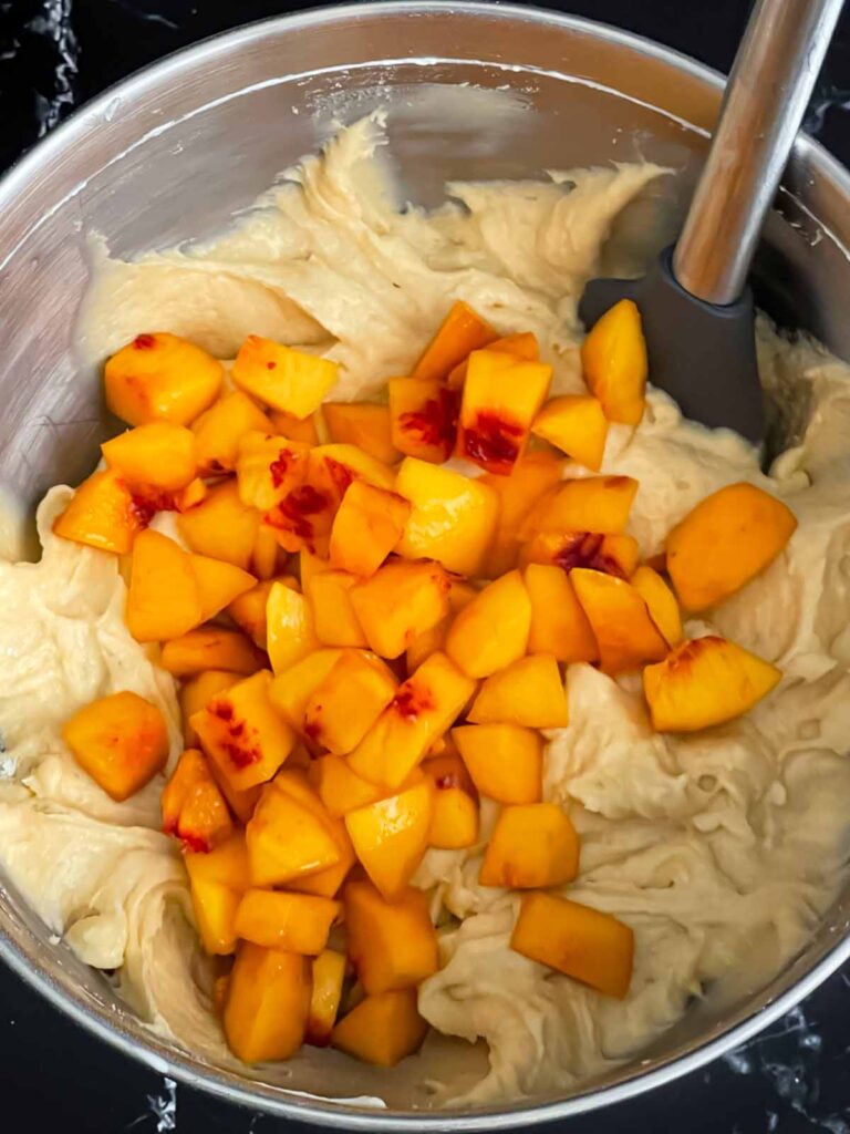 Peach chunks added to the peach pound cake batter in a metal mixing bowl.