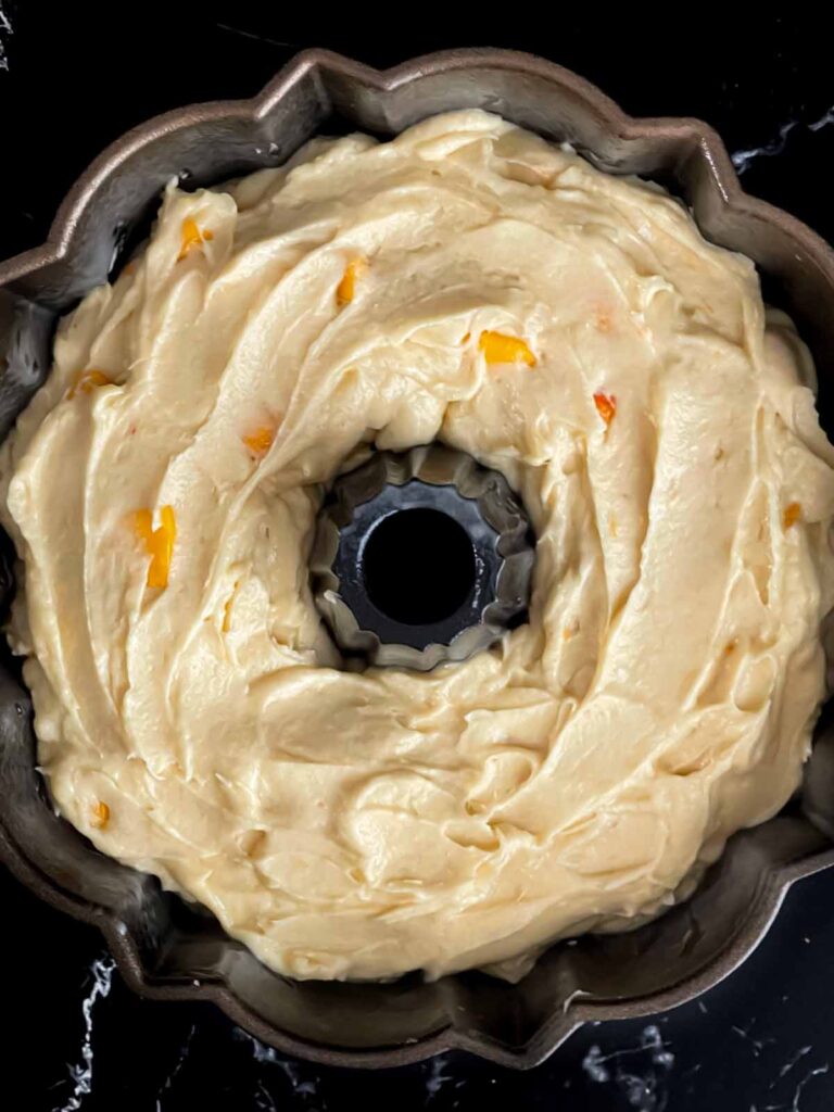 Peach pound cake batter in a bundt pan on a dark surface.