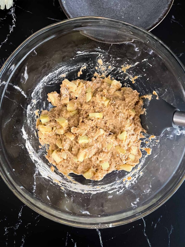 Apple fritters batter mixed in a glass mixing bowl on a dark surface.