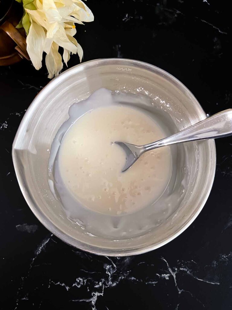 Apple fritters glaze mixed in a metal bowl on a dark surface.