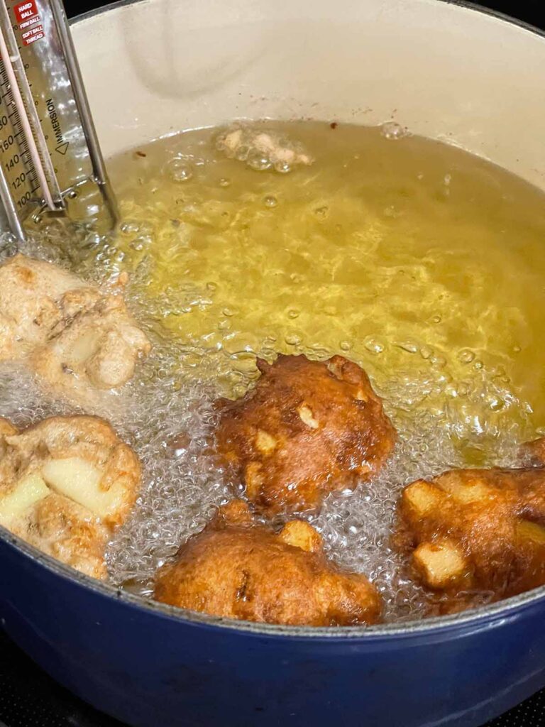 Apple fritters frying in a large dutch oven.