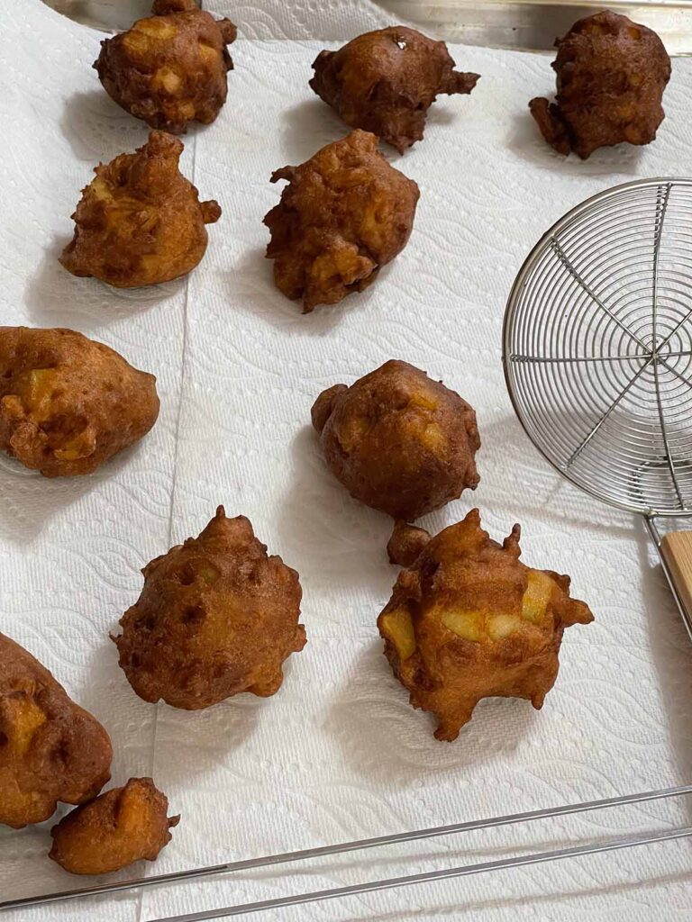 Fried apple fritters on a paper towel lined baking sheet.