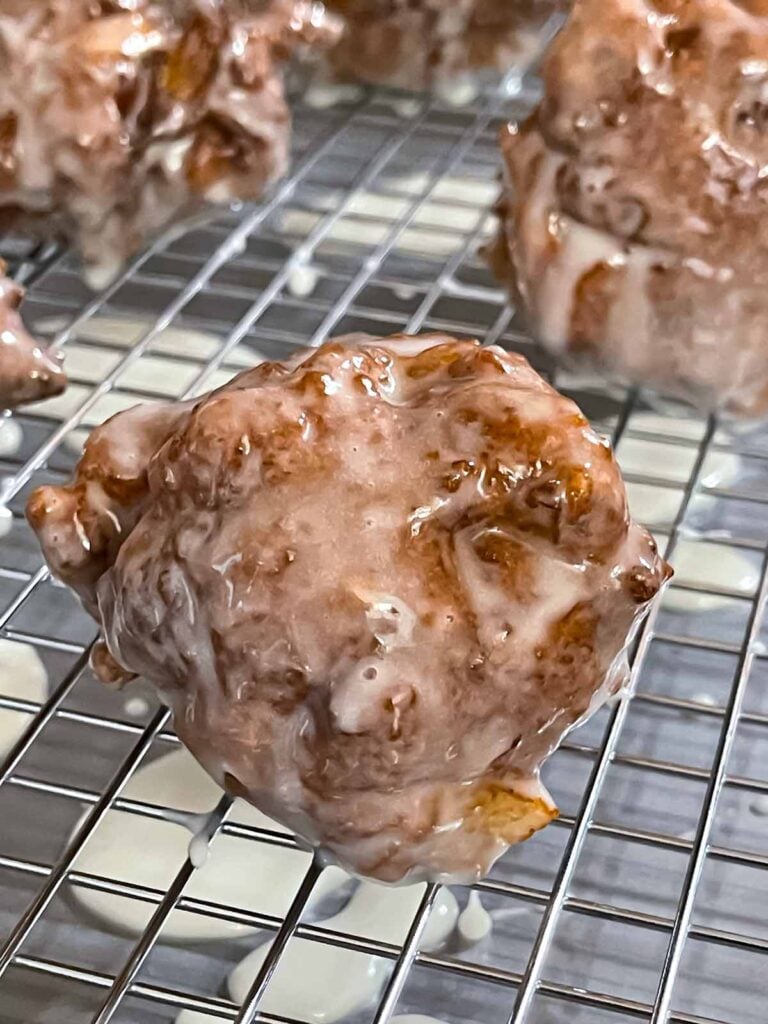 Glazed apple fritters on a wire rack over a baking sheet.