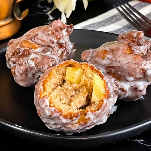 Apple fritters on a dark plate on a dark surface.