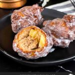 Apple fritters on a dark plate on a dark surface.