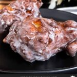 Apple fritters on a dark plate on a dark surface.