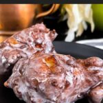 Apple fritters on a dark plate on a dark surface.