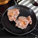 Apple fritters on a dark plate on a dark surface.