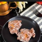 Apple fritters on a dark plate on a dark surface.