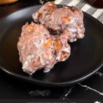 Apple fritters on a dark plate on a dark surface.