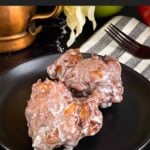 Apple fritters on a dark plate on a dark surface.