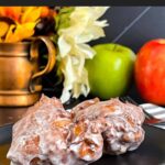 Apple fritters on a dark plate on a dark surface.