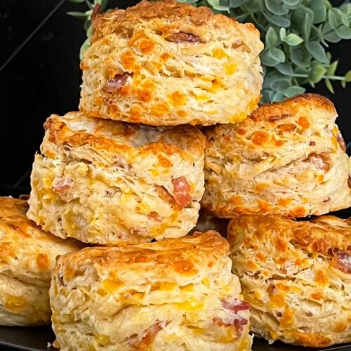 Bacon cheddar biscuits stacked on a dark plate.